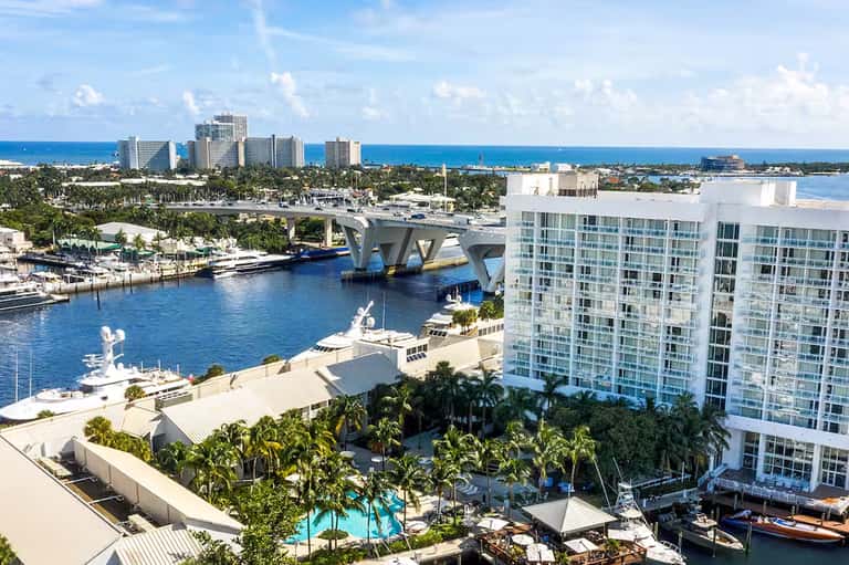 Waterfront resort with white high-rise hotel, marina, pools, and ocean views in tropical setting