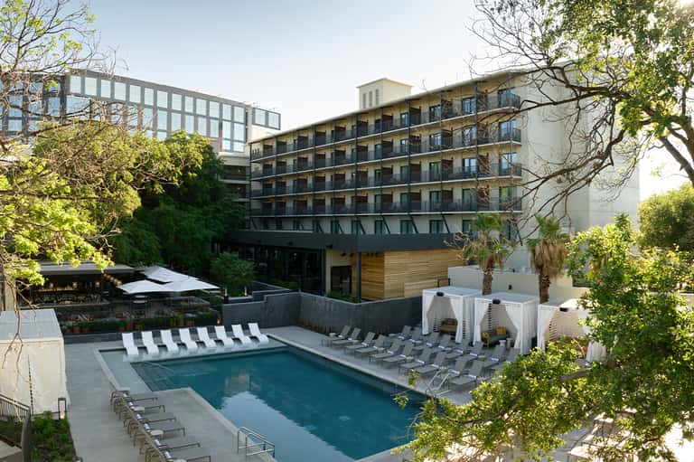 Modern hotel building with pool surrounded by lounge chairs and tropical landscaping during daytime