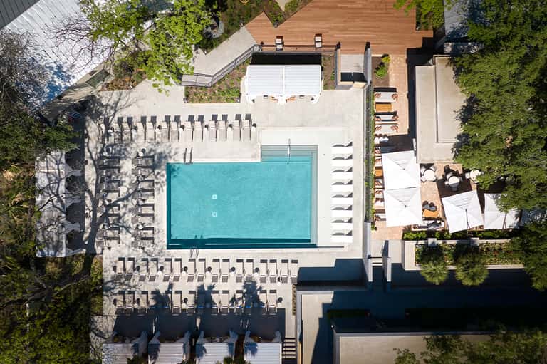 Aerial view of resort pool surrounded by loungers, buildings, and manicured landscaping