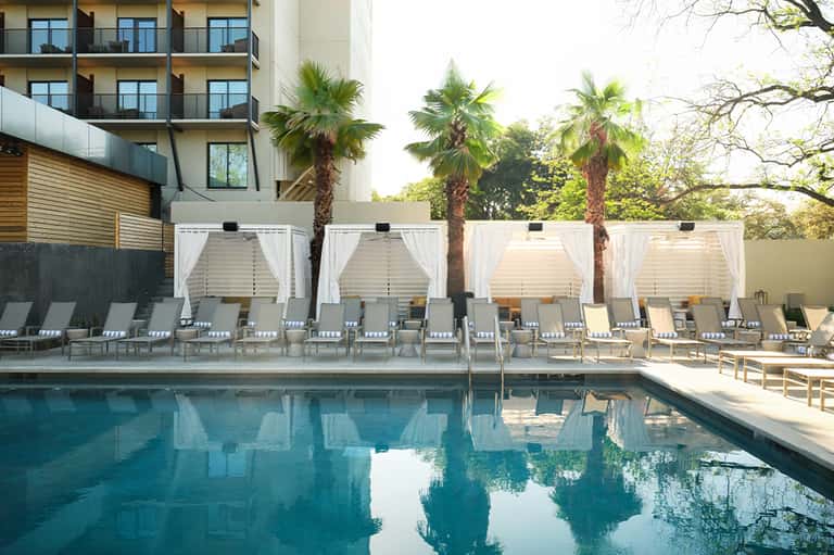 Resort pool with turquoise water, white cabanas, palm trees, and modern hotel building