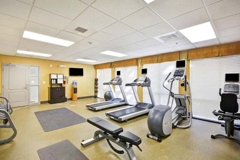 Modern fitness center with yellow walls, treadmills, exercise bikes, and equipment with monitors in a bright, spacious room.