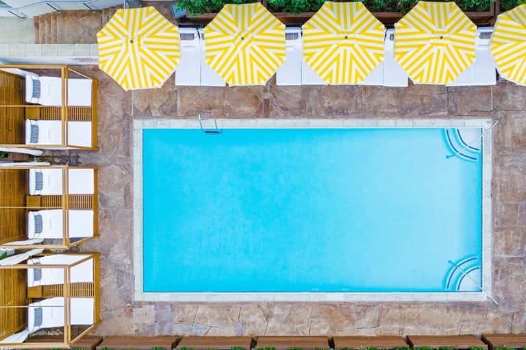 Overhead view of rectangular swimming pool with bright yellow and white striped umbrellas and cabanas