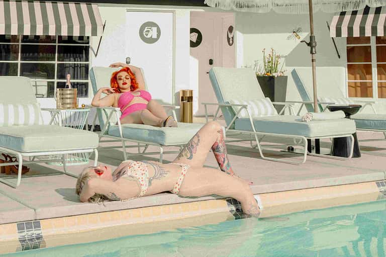 Vintage-style outdoor pool area with retro lounge chairs, striped umbrellas, and guests in 1950s-inspired swimwear