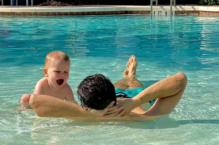 Adult and toddler playing in shallow turquoise pool water at resort