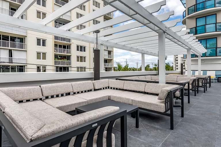 Modern rooftop terrace with sectional seating, fire pit, pergola structure, and city views