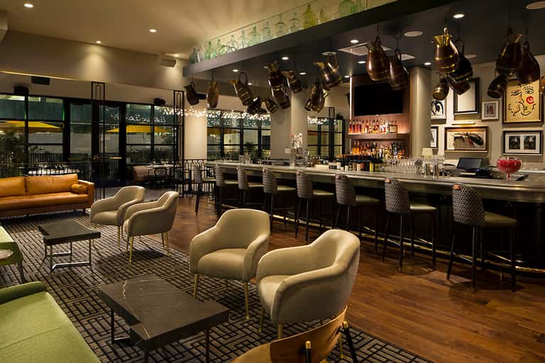 Modern hotel bar lounge with cream armchairs, brass pendant lights, and panoramic windows