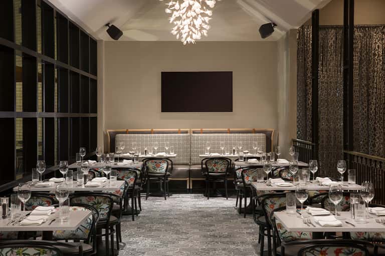 Elegant dining room with long tables, patterned chairs, beige banquette seating, and modern chandelier