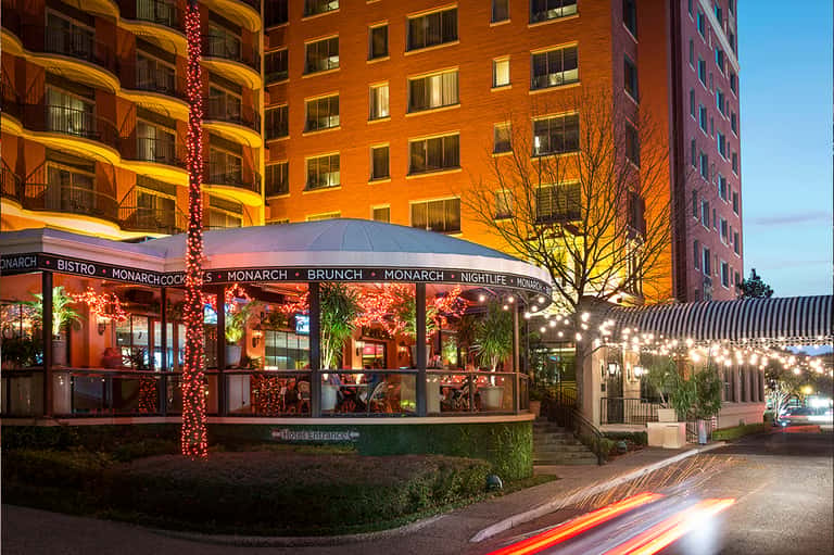 Hotel bistro and nightlife venue at dusk with warm lighting, decorated columns, and brick building facade