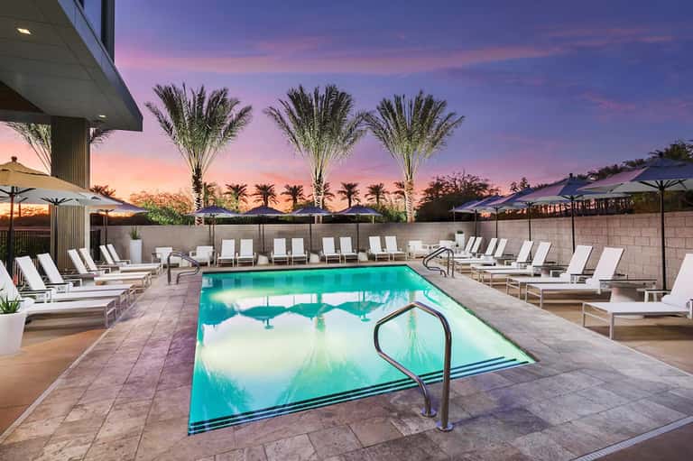 Luxury resort pool at sunset with palm trees, lounge chairs, and umbrellas under purple sky