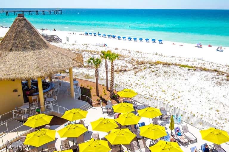 Beach resort with white sand, blue umbrellas, thatched-roof bar, and turquoise ocean waters