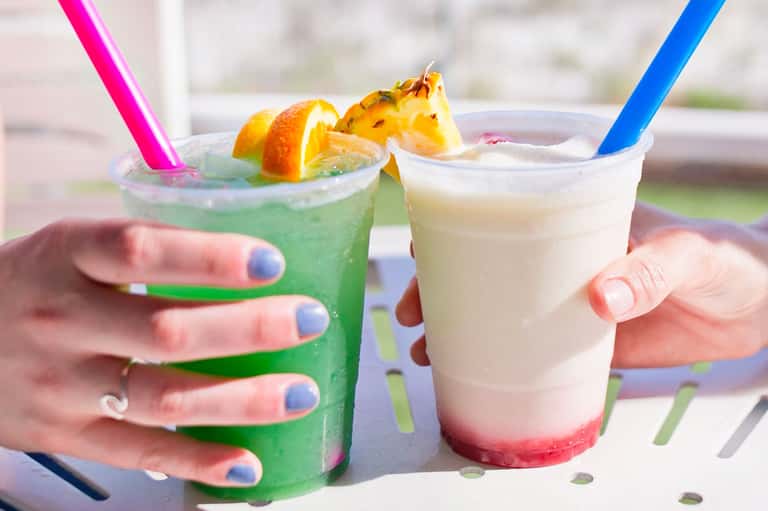 Two colorful tropical cocktails with pineapple garnish and straws held in hands outdoors