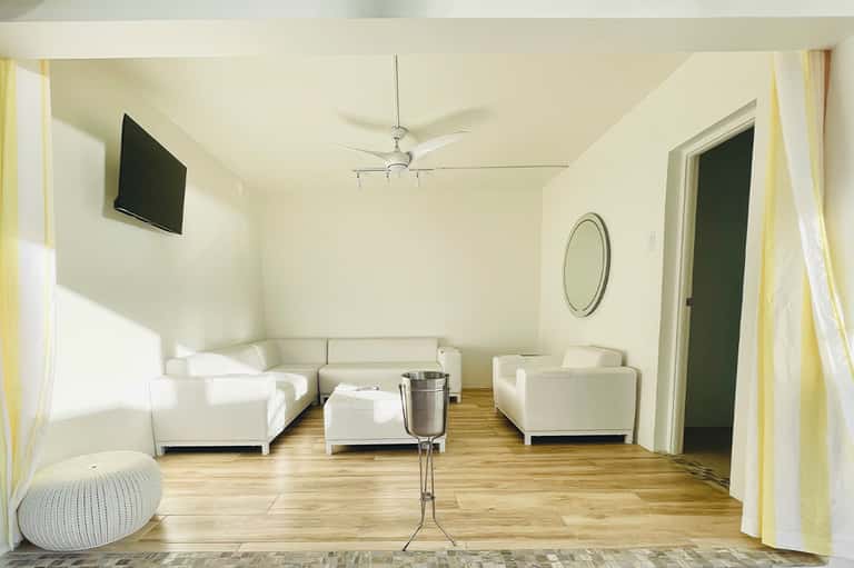 Modern lounge with white sofas, wooden floor, ceiling fan, and minimalist décor
