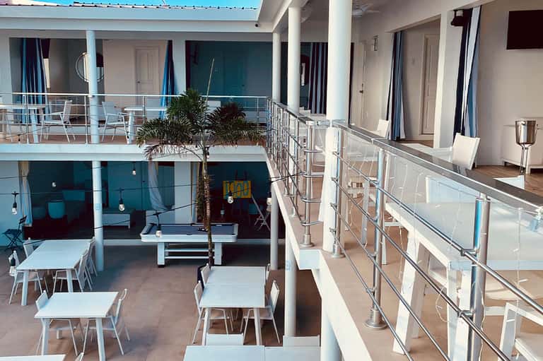 Modern hotel courtyard with multi-level white railings, dining tables, and tropical plants