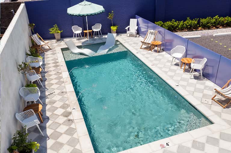 Outdoor pool deck with turquoise lap pool, lounge chairs, umbrellas, and modern white chairs