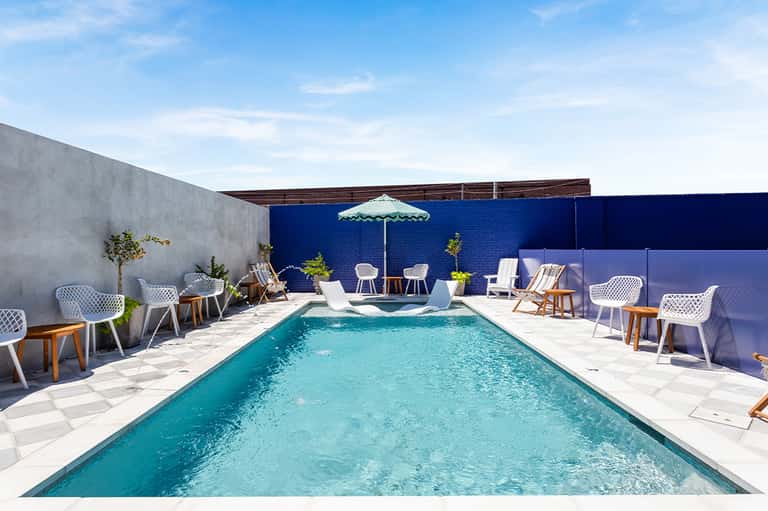 Resort rooftop pool with turquoise water, white loungers, blue umbrellas, and contemporary outdoor seating