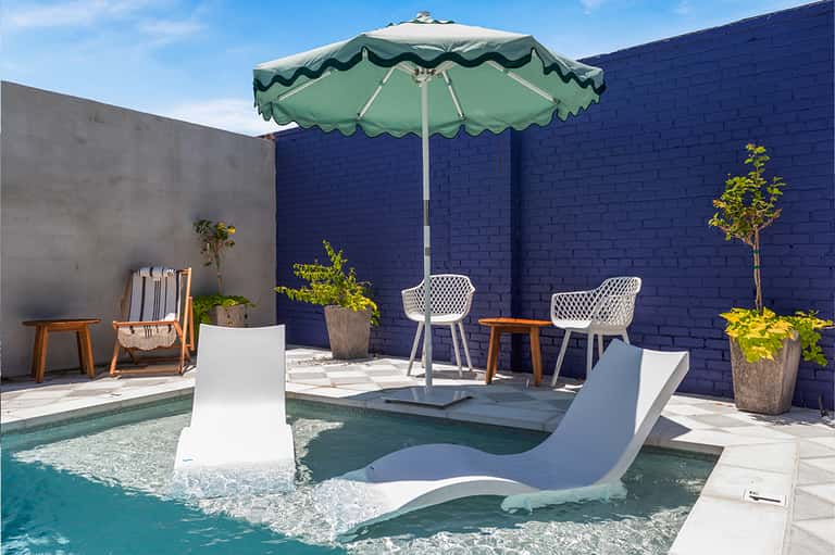 Resort courtyard with small pool, white loungers, green umbrella, and navy brick walls