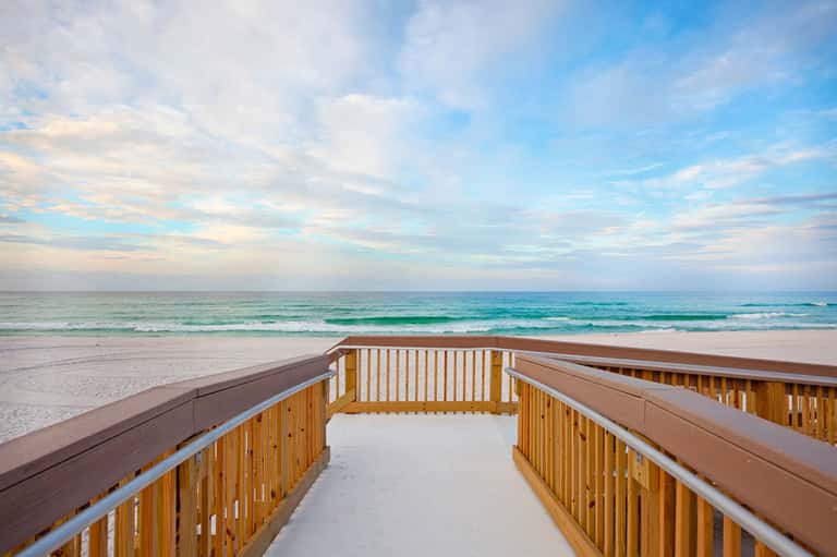 Wooden boardwalk leading to pristine beach with turquoise ocean and cloudy sky