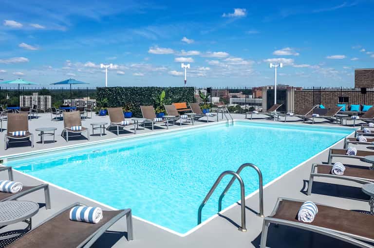 Rooftop pool with bright blue water, lounge chairs, and city skyline views under clear blue sky