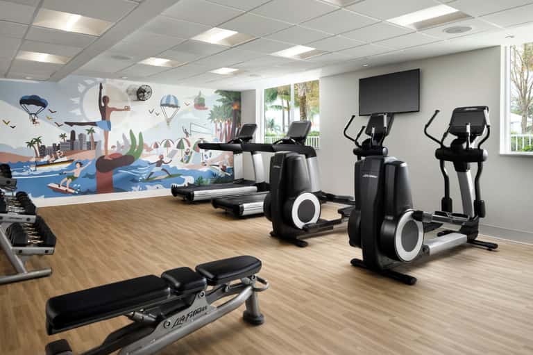 Modern fitness center with cardio equipment, colorful mural, and wooden flooring