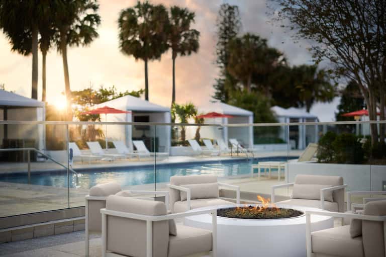 Resort pool at sunset with white fire pit seating, palm trees, and cabanas
