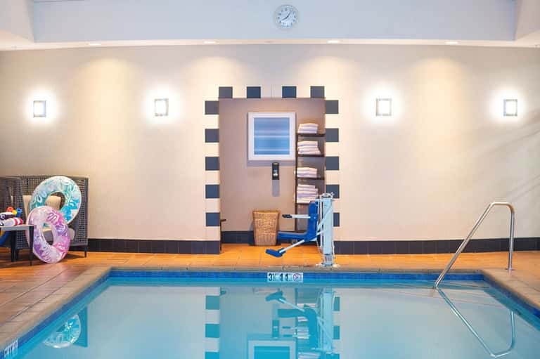 Indoor swimming pool with lane markings, decorative tile wall, and modern lighting fixtures