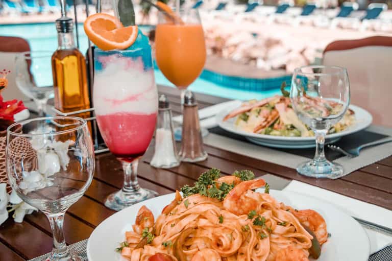 Beachfront dining table with shrimp appetizer, tropical cocktails, and ocean view under blue sky