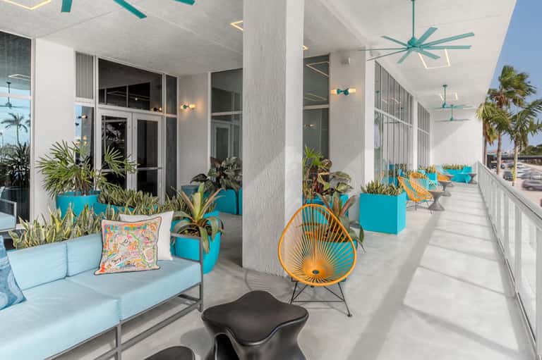 Bright coastal terrace with turquoise planters, white columns, ceiling fans, and ocean views