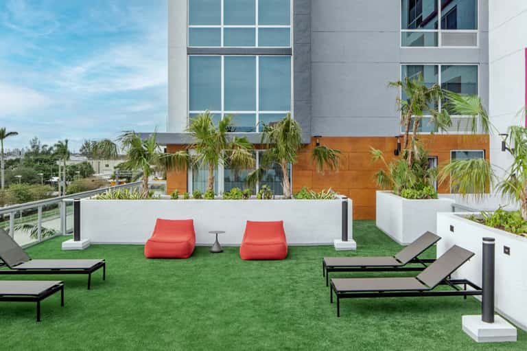 Modern rooftop terrace with red bean bag chairs, lounge chairs, and palm trees overlooking city