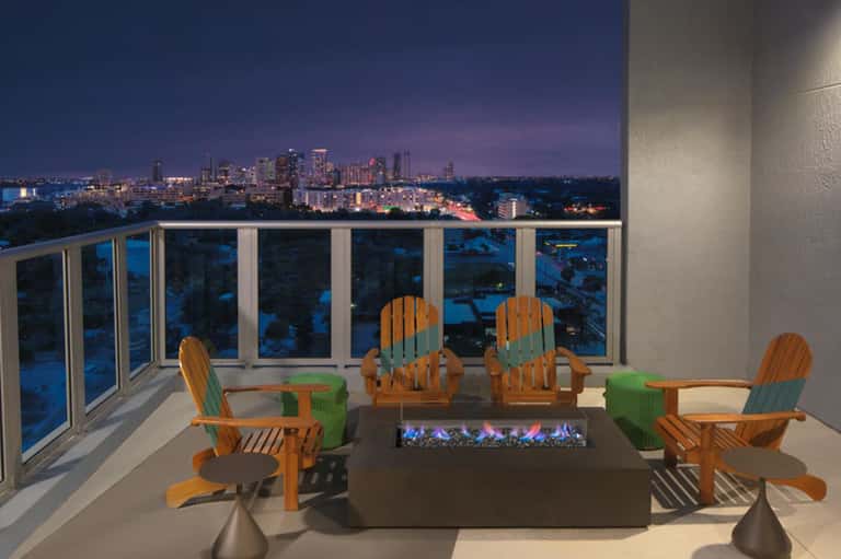 High-rise balcony with fire pit, Adirondack chairs, and city skyline view at dusk