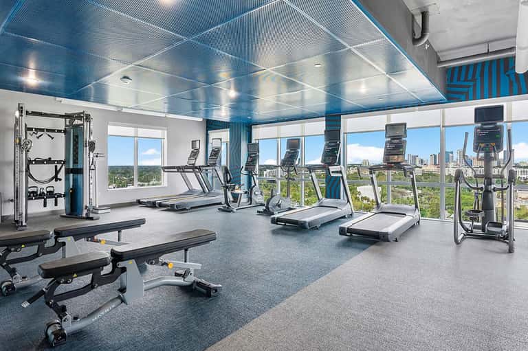 Modern fitness center with cardio equipment, weights, and floor-to-ceiling windows overlooking cityscape