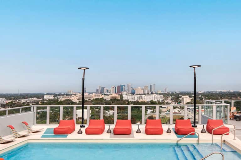 Rooftop pool area with red loungers, heaters, and city skyline view in the distance
