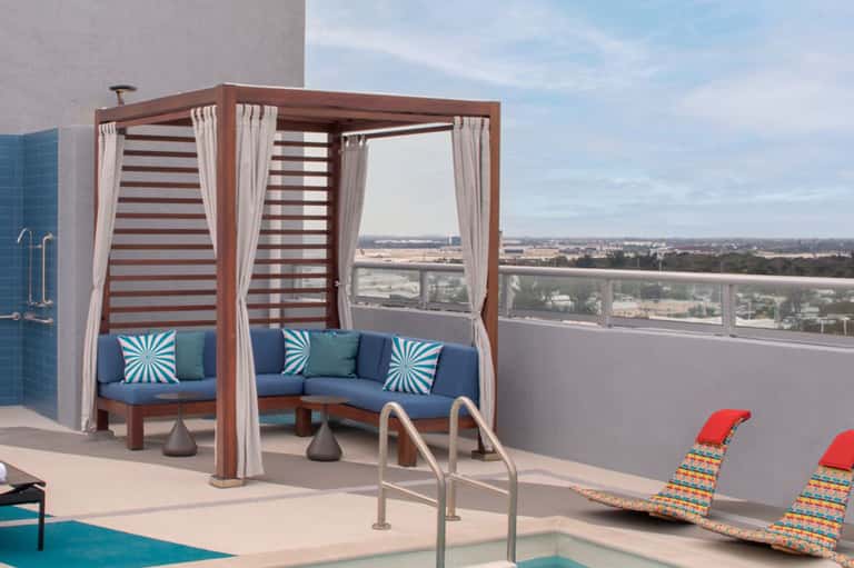 Rooftop lounge with striped cabana, blue seating, and panoramic cityscape views