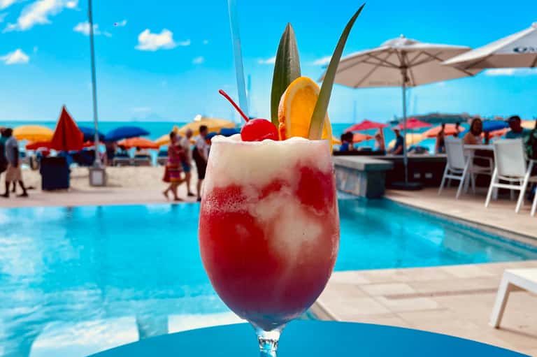 Tropical cocktail with fruit garnish by resort pool and beach umbrellas