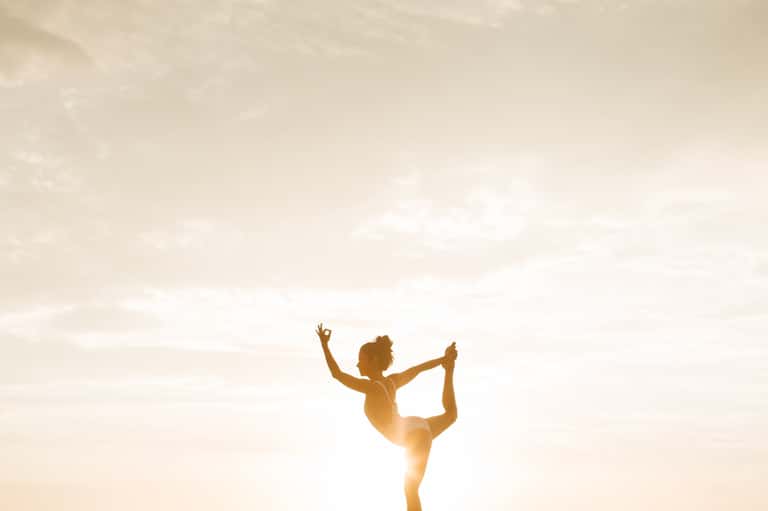 Woman in yoga pose silhouetted against golden sunset sky