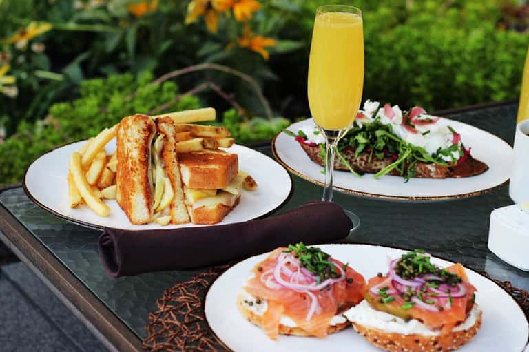 Outdoor dining spread with smoked salmon toast, French fries, and champagne in garden setting
