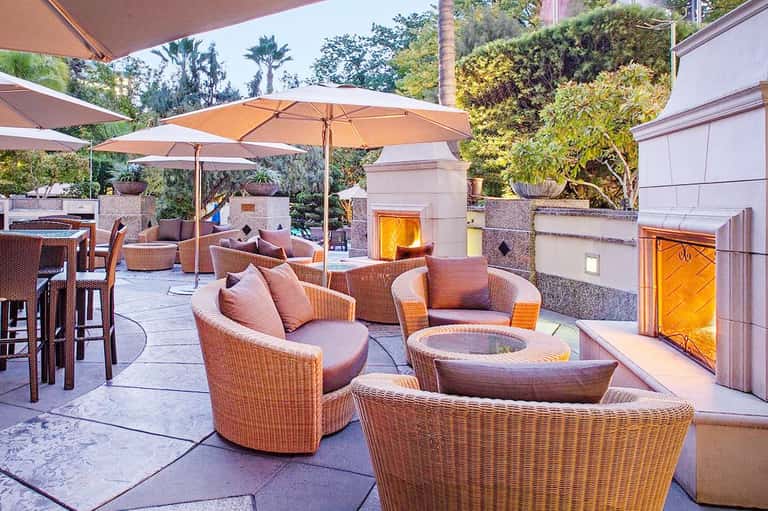 Upscale outdoor patio with wicker seating, fire pit, umbrellas, and palm trees