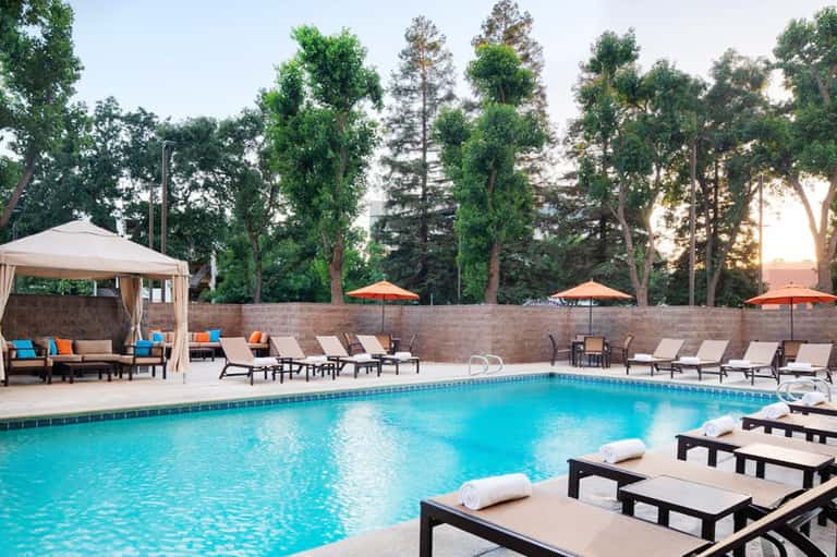 Luxury resort pool with turquoise water, lounge chairs, orange umbrellas, and tall trees at dusk