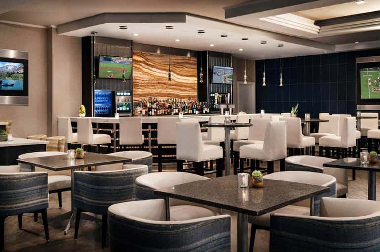 Modern upscale lounge with bar, white seating, dark accent walls, and multiple televisions