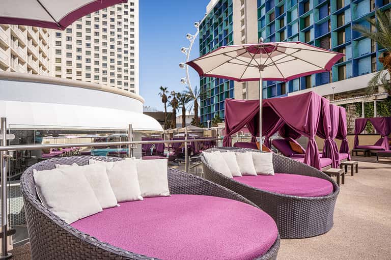 Rooftop pool deck with pink and burgundy lounge chairs, umbrellas, and modern high-rise buildings