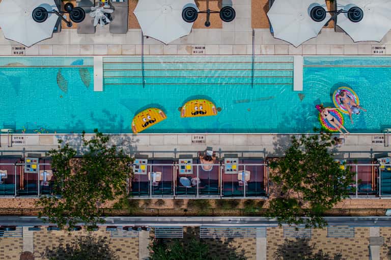 Aerial view of resort pool with colorful floats and white umbrellas overlooking the beach