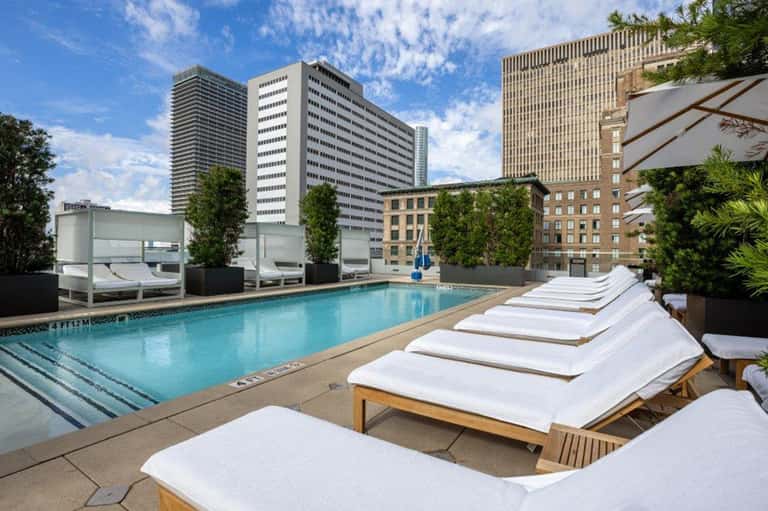 Rooftop pool with lounge chairs and city skyline views surrounded by modern high-rise buildings