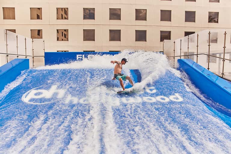 Indoor surfing facility with person riding artificial wave in blue pool with foam