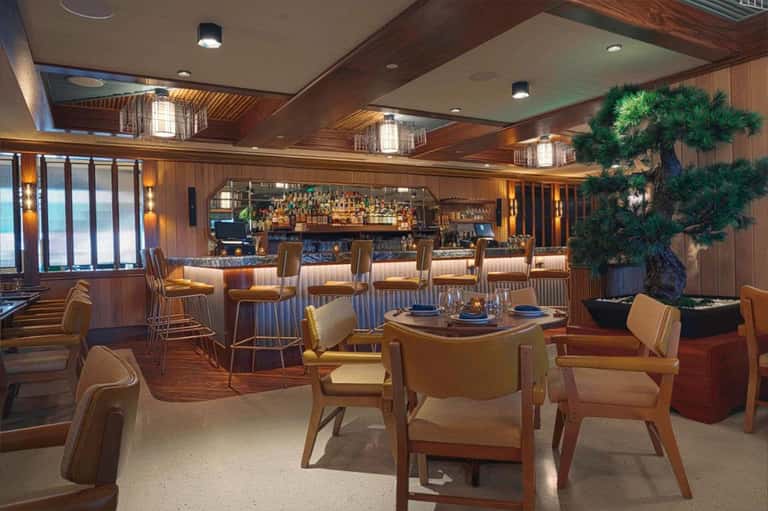 Upscale bar lounge with wood paneling, bonsai tree, leather seating, and well-stocked liquor shelves