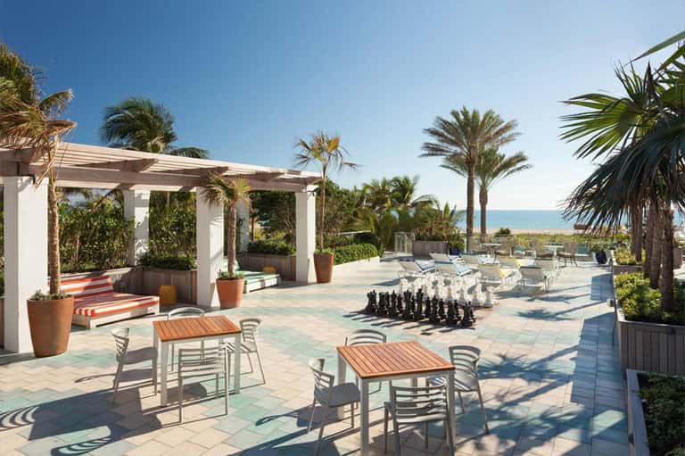 Beachfront terrace with palm trees, pergola, lounge chairs, and ocean view