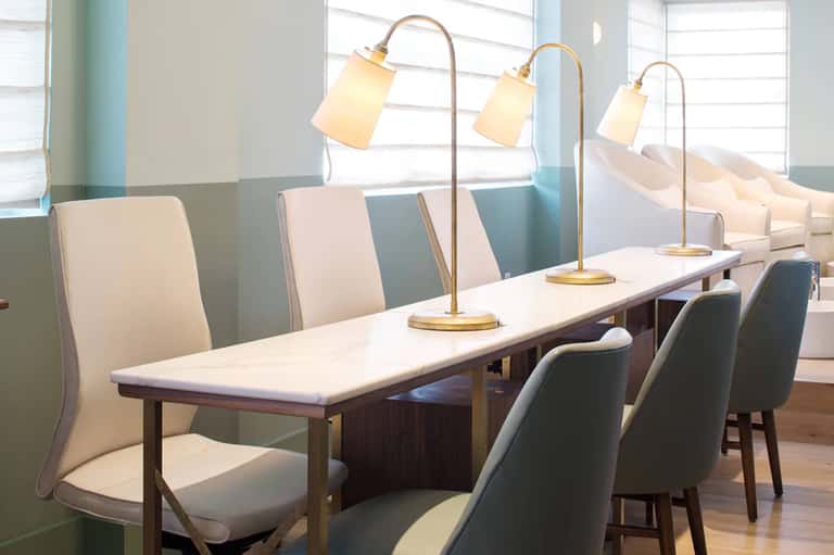 Modern dining room with long white table, brass arc lamps, and upholstered chairs by large windows