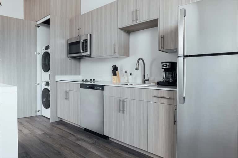 Modern kitchen with gray wood cabinetry, stainless steel appliances, and stacked washer/dryer units