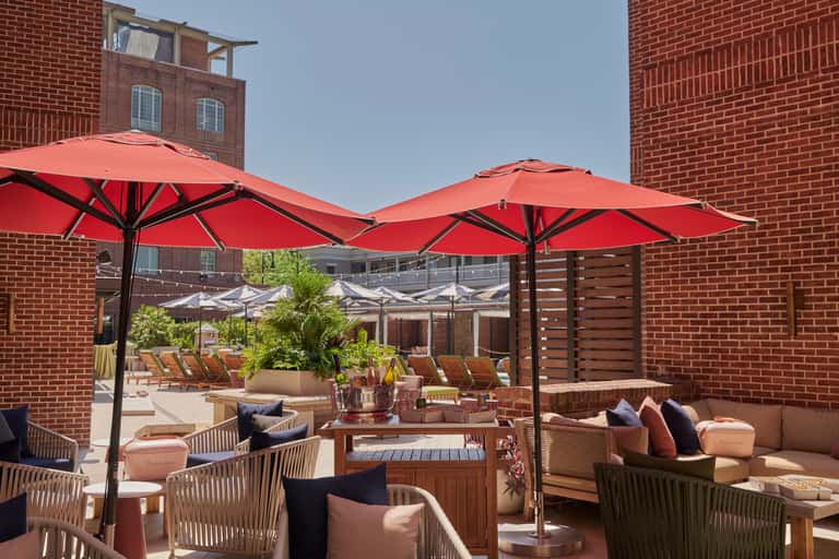 Rooftop terrace with red umbrellas, wicker seating, and brick building backdrop