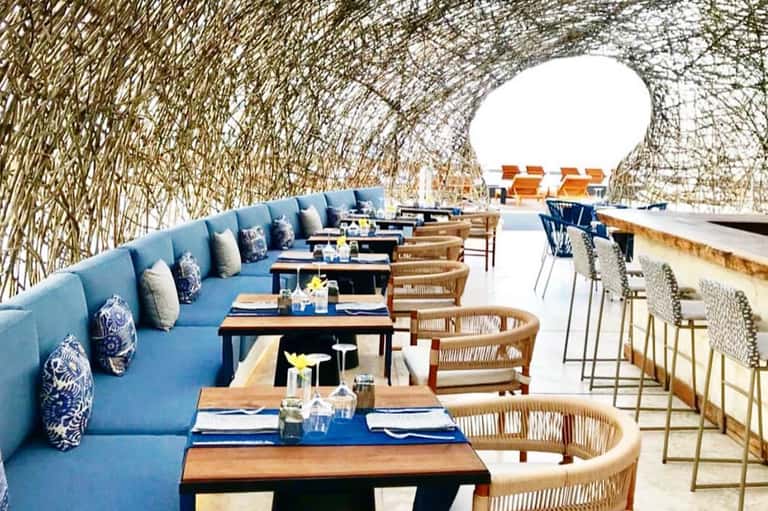 Modern restaurant terrace with blue banquette seating, woven chairs, and reed wall screening