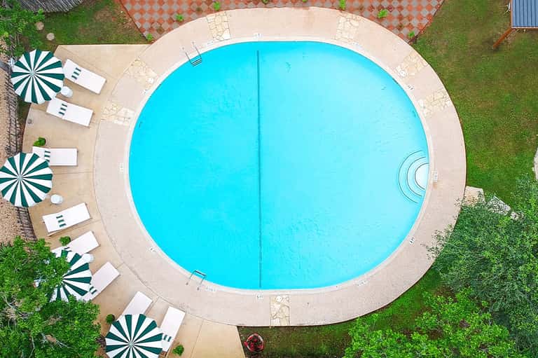 Aerial view of circular turquoise swimming pool with beige deck and green umbrellas with lounge chairs
