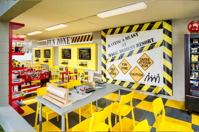 Bright yellow and black kids fun zone with arcade games, activity tables, and construction-themed decor